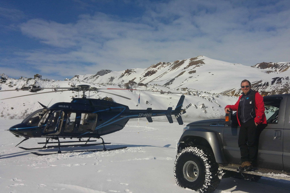 Blått helikopter og grå super jeep står på snø, en person ved bilen