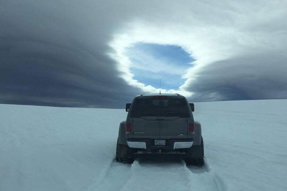 Grå pickup sett bakfra på en snøslette under en stor linseformet sky