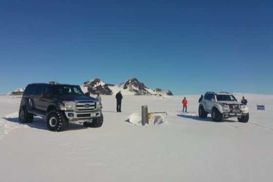To super jeeper parkert på snø under skyfri blå himmel med snødekte fjell bak